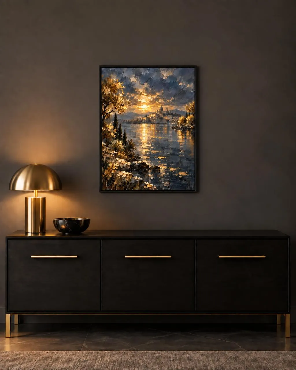 Obra de un atardecer sobre el lago, enmarcada en negro sobre un aparador oscuro junto a una lámpara dorada